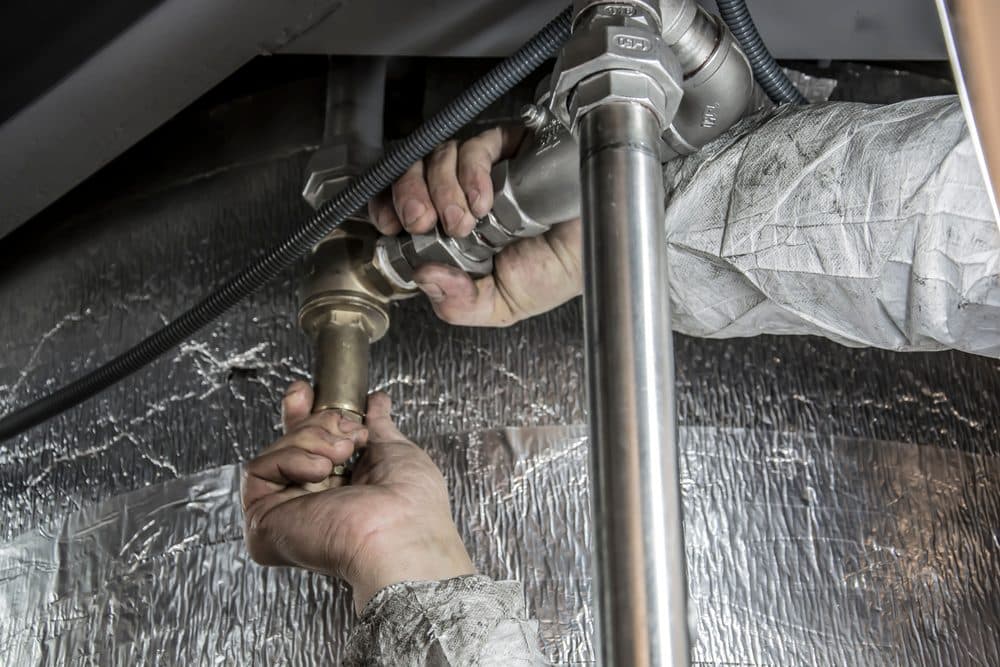 Técnico ajustando con llave una tubería para localizar una fuga de agua
